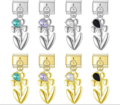 A 9mm Italian charm featuring a sleek metal flower dangle with a teardrop crystal accent. Available on silver and gold bases with teal, purple, clear, and black gems.