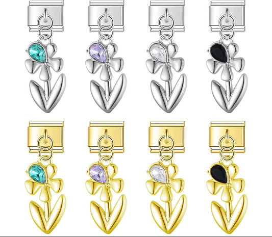 A 9mm Italian charm featuring a sleek metal flower dangle with a teardrop crystal accent. Available on silver and gold bases with teal, purple, clear, and black gems.