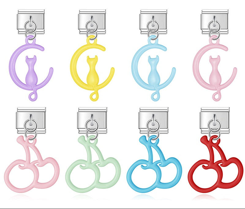 A 9mm silver Italian charm featuring a glossy, open-cutout dangle of either a cat on a moon or a pair of cherries. Available in pastel purple, yellow, blue, pink, green, and red.